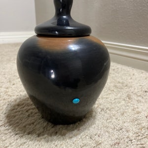 May include: A black and brown ceramic jar with a lid and a turquoise stone accent. The jar has a smooth, glossy finish.