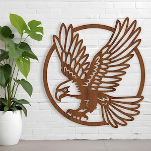 May include: A brown wooden eagle with its wings spread wide, in a circular frame, against a white brick wall background.