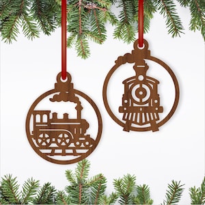May include: Two wooden Christmas ornaments shaped like trains, hanging from red ribbons. The ornaments are brown and feature detailed cut-out designs of steam locomotives within circular frames. Green pine branches frame the ornaments.