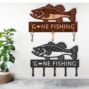 May include: A wooden wall-mounted key holder with a black and brown bass fish design. The key holder has the text "Gone Fishing" and five hooks for hanging keys.