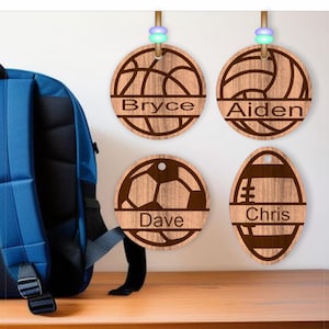 May include: Four wooden personalized name tags with different sports ball designs. The tags are hanging from a string and feature the names Bryce, Aiden, Dave, and Chris.