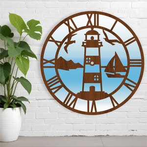 Puede incluir: Un reloj de madera marrón con un faro, un velero y gaviotas recortadas sobre un fondo degradado azul y blanco. La esfera del reloj tiene números romanos.