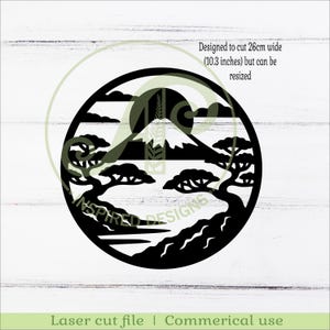May include: Black laser-cut design of a mountain landscape within a circle. The design includes trees, a mountain, a sun, and clouds. The text says "Designed to cut 10.3 inches wide but can be resized." The bottom text says "Laser cut file | Commerical use."