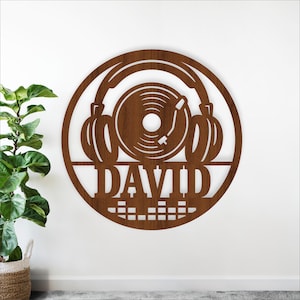 May include: A wooden wall art piece featuring a turntable record player design with headphones and the name "DAVID" cut out. The artwork is circular and has a brown finish, suitable for music enthusiasts.