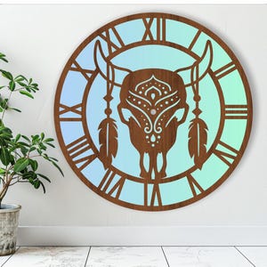 May include: A wooden wall clock with a blue and green gradient background. The clock face features a stylised bull skull with intricate details and a feather design. The clock has Roman numeral markings.