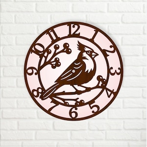 May include: A round wooden wall clock featuring a detailed cutout design of a cardinal bird perched on a branch. The clock face has a light pink background with brown numerals and a brown outer ring. The clock is mounted on a white brick wall.