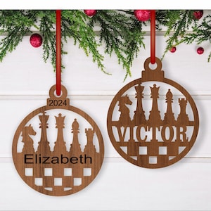 May include: Two wooden Christmas ornaments shaped like a circle with a chessboard pattern. The ornaments feature a silhouette of chess pieces and the names "Victor" and "Elizabeth" with the year "2024" on one ornament.