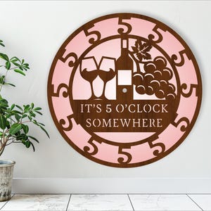 May include: A pink and brown wooden wall clock with the text "It's 5 o'clock somewhere" and a design of two wine glasses and a bottle of wine with grapes.