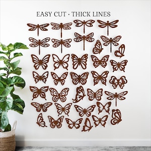 Op de afbeelding: Bruine metalen wandkunst met libellen en vlinders in verschillende maten en ontwerpen. De tekst "EASY CUT • THICK LINES" staat bovenaan. De kunst is op een witte muur gemonteerd.