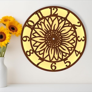 May include: A round wooden clock with a sunflower design. The clock face is yellow with brown numbers and a brown sunflower in the center. The clock is hanging on a white wall.