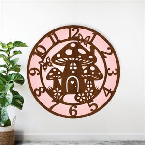Op de afbeelding: Een ronde houten klok met een grillig paddenstoelenhuisontwerp. De wijzerplaat is lichtroze, met bruine cijfers en een bruin paddenstoelenhuissilhouet. Vlinders en bloemen voegen decoratieve details toe. De klok is aan een witte muur bevestigd.