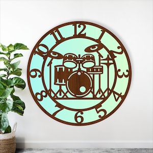 Op de afbeelding: Een ronde houten wandklok met een drumstel-silhouet. De klok heeft een lichtblauwe tot groene gradiënt, met bruine cijfers en een bruin drumstelontwerp. Een decoratief item voor muziekliefhebbers.