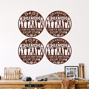 May include: Four circular brown wall signs featuring cut-out tool silhouettes including a hammer, wrench, and saw. Each sign displays the text WORKSHOP and the phrase I CAN FIX ANYTHING EXCEPT STUPID, with variations for DAD'S, GRANDAD'S, POP'S, and GRANDPA'S.