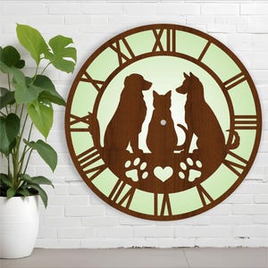 Könnte beinhalten: Eine braune Holzuhr mit hellgrünem Hintergrund. Das Zifferblatt der Uhr zeigt römische Ziffern und eine Silhouette von zwei Hunden und einer Katze. Die Uhr hat ein Herz und Pfotenabdrücke unter den Tieren.