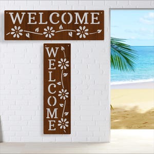 Puede incluir: Dos letreros de madera con la palabra "WELCOME" en letras blancas. El letrero superior es un rectángulo horizontal con un diseño de vid y flores. El letrero inferior es un rectángulo vertical con la palabra "WELCOME" deletreada verticalmente con un diseño de vid y flores.