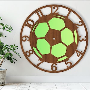 Könnte beinhalten: Eine Holzuhr mit einem Fußball-Design. Das Zifferblatt der Uhr ist braun mit einem grünen Fußball in der Mitte. Die Zahlen 1 bis 12 befinden sich am Rand des Zifferblatts.