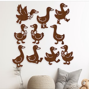 May include: A collection of wooden duck wall decorations in various poses, including flying and walking. The ducks are a warm brown colour and are mounted on a white wall. The art adds a whimsical touch to any room.