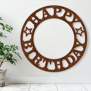 Pode incluir: Um círculo de madeira marrom com as palavras "Happy Birthday" cortadas ao redor da borda. O círculo está pendurado em uma parede branca.