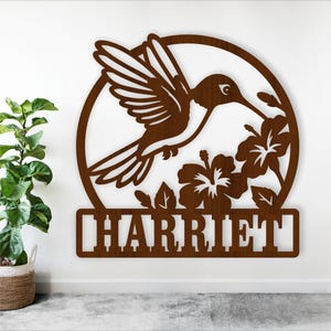 May include: A brown wooden cutout of a hummingbird with flowers and the name "HARRIET" underneath.
