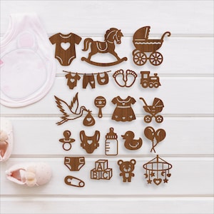 May include: Wooden baby-themed cutouts in various shapes, including a rocking horse, baby carriage, and clothing. The cutouts are brown and arranged on a white surface, with a bib and baby shoes in the background.
