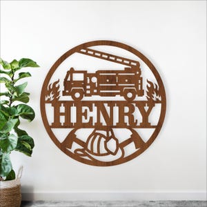 Peut inclure: Décoration murale en bois marron représentant un camion de pompiers, des flammes et le nom "HENRY" dans un cercle. Le design inclut un casque de pompier et des haches. Idéal pour une chambre d'enfant.