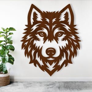 Op de afbeelding: Een bruine houten wolfskop silhouet wanddecoratie. De wolfskop is naar voren gericht met de mond gesloten. De vacht van de wolf is gedetailleerd met ingewikkelde sneden.