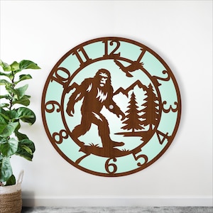May include: A round wooden wall clock with a light blue background. The clock features a brown silhouette of Bigfoot, mountains, trees, and a flying bird. The numbers are cut out of the wood. The clock measures approximately 46 cm in diameter.