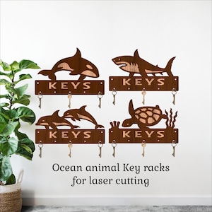 May include: Wooden key racks featuring ocean animals: an orca, shark, dolphins, and a sea turtle. Each rack has the word "KEYS" and several key hooks. The text "Ocean animal Key racks for laser cutting" is below the racks.