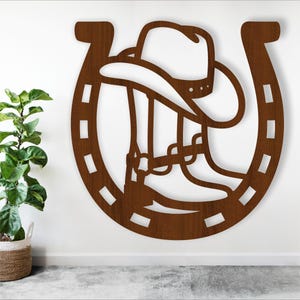 May include: A brown wooden cutout of a cowboy boot and hat inside a horseshoe. The horseshoe is outlined with a dashed line.