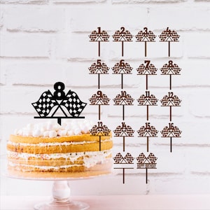 May include: A layered cake with a black and white checkered flag cake topper with the number 8. Additional brown cake toppers with checkered flags and numbers 1-16 are also displayed. The words "Happy Birthday" are also displayed.