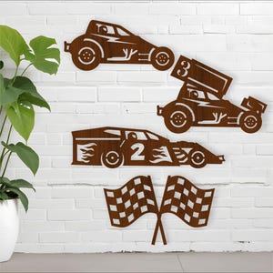 Könnte beinhalten: Braune Metall-Wandkunst mit drei Rennwagen und zwei Zielflaggen. Die Rennwagen sind in verschiedenen Stilen gehalten, mit den Zahlen 2 und 3 sichtbar. Die Kunst ist an einer weißen Backsteinmauer angebracht.