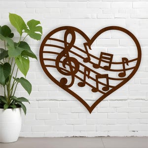 Könnte beinhalten: Braune Metall-Wandkunst in Herzform mit Noten und einem Violinschlüssel. Das Kunstwerk ist an einer weißen Backsteinmauer angebracht, mit einer Topfpflanze auf der linken Seite.
