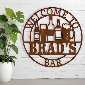 Może przedstawiać: Brązowy metalowy znak z tekstem "Witamy w barze Brada" w kółku. Znak przedstawia sylwetkę baru z butelkami piwa i szklankami.