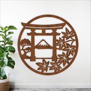 May include: A wooden wall art piece featuring a Japanese torii gate, Mount Fuji, and maple leaves, all within a circular frame. The artwork is a warm brown color and has a cut-out design. A small tree is also included in the design.