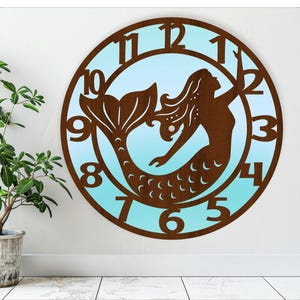 May include: A brown wooden clock with a mermaid silhouette and blue and white ombre background. The clock face has Roman numerals.