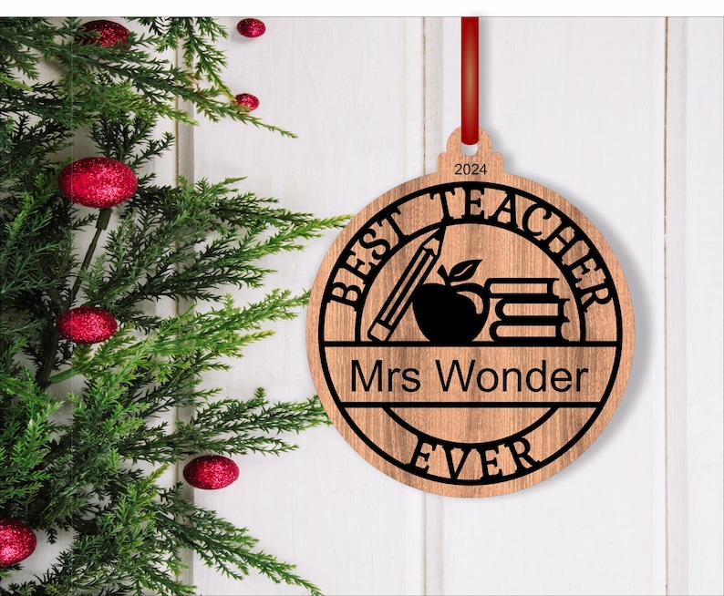 Może przedstawiać: Okrągła drewniana ozdoba z tekstem "Best Teacher Ever" i "Mrs. Wonder" w czarnym k&oacute;łku. Ozdoba zawiera r&oacute;wnież oł&oacute;wek, jabłko i książki.