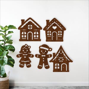 May include: Four wooden Christmas decorations: two gingerbread houses and two gingerbread people. The gingerbread houses have arched doorways and decorative windows. The gingerbread people are a boy and a girl, each with a unique design.