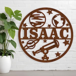 Könnte beinhalten: Ein rundes Schild aus braunem Holz mit Weltraumthema. Das Schild zeigt ein Teleskop, Planeten, Sterne und den Namen "ISAAC".