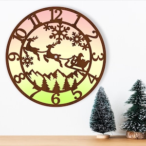Può includere: Un orologio di Natale in legno con uno sfondo sfumato di rosa, giallo e verde. Il quadrante dell'orologio presenta una silhouette di Babbo Natale nella sua slitta trainata da renne, che vola sopra un paesaggio montano innevato. I numeri dell'orologio sono in un carattere marrone.