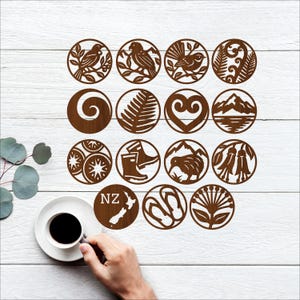 Puede incluir: Dieciséis recortes circulares de madera en marrón, cada uno con un diseño diferente. Los diseños incluyen pájaros, helechos y un mapa de Nueva Zelanda con el texto "NZ".