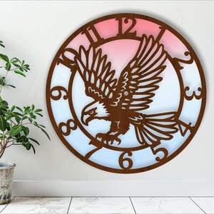 May include: A brown wooden clock with a silhouette of an eagle flying with its wings spread. The clock face has a pink and blue gradient background with Roman numeral markings.