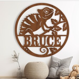May include: A brown wooden round sign with a cutout of a chameleon on a branch. The sign has the name "Bruce" written in a decorative font.