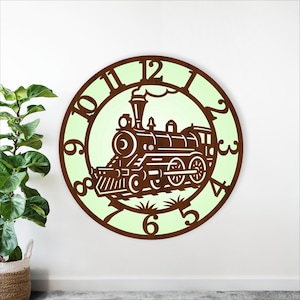 Puede incluir: Un reloj de pared redondo con un diseño de tren marrón dentro de un círculo verde claro. La esfera del reloj tiene números y manecillas marrones, con los detalles del tren recortados. El reloj está montado en una pared blanca.