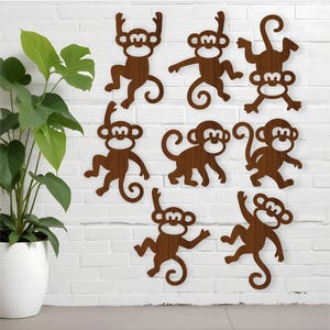 May include: Nine wooden monkey wall decorations in various poses are mounted on a white brick wall. A potted plant with large green leaves is on the left. The monkeys are brown with white faces.