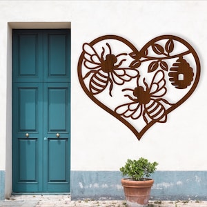 May include: A brown metal heart-shaped wall art piece featuring two bees, a beehive, and leaves. The artwork is mounted on a white wall next to a teal door and a potted plant.