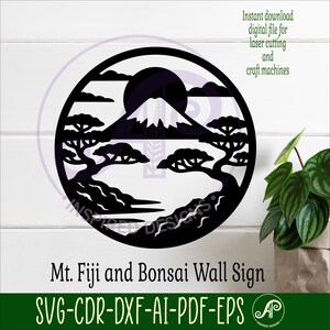 May include: A black, circular wall sign featuring a silhouette of Mount Fuji, bonsai trees, and a rising sun. The sign includes the text "Mt. Fuji and Bonsai Wall Sign" and file type information. The design is suitable for laser cutting.