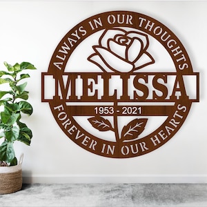 May include: Brown wooden circle with the text "Always in our thoughts forever in our hearts" surrounding a white rose with a stem and leaves. The name "Melissa" is written in a banner across the bottom with the dates "1953 - 2021" below.