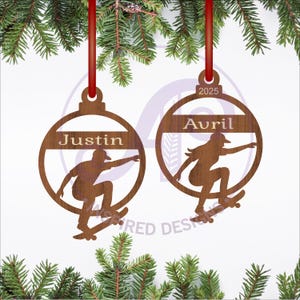 Puede incluir: Dos adornos navideños de madera con cintas rojas. Cada adorno presenta una silueta de patinador dentro de un marco circular. Uno dice "Justin", el otro "Avril" y "2025".