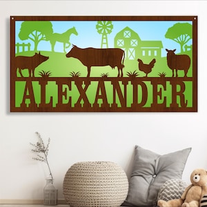 Puede incluir: Un letrero de madera marrón con un fondo verde y azul que presenta animales de granja, un granero y un molino de viento. El nombre "ALEXANDER" está escrito en letras marrones en el letrero.