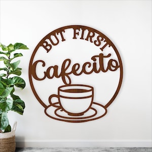Könnte beinhalten: Braune Wanddekoration aus Holz mit dem Schriftzug "BUT FIRST Cafecito" in einem kreisförmigen Design. Eine Kaffeetasse und Untertasse befinden sich in der Mitte. Die Kunst ist aus Holz geschnitten und an einer weißen Wand befestigt.